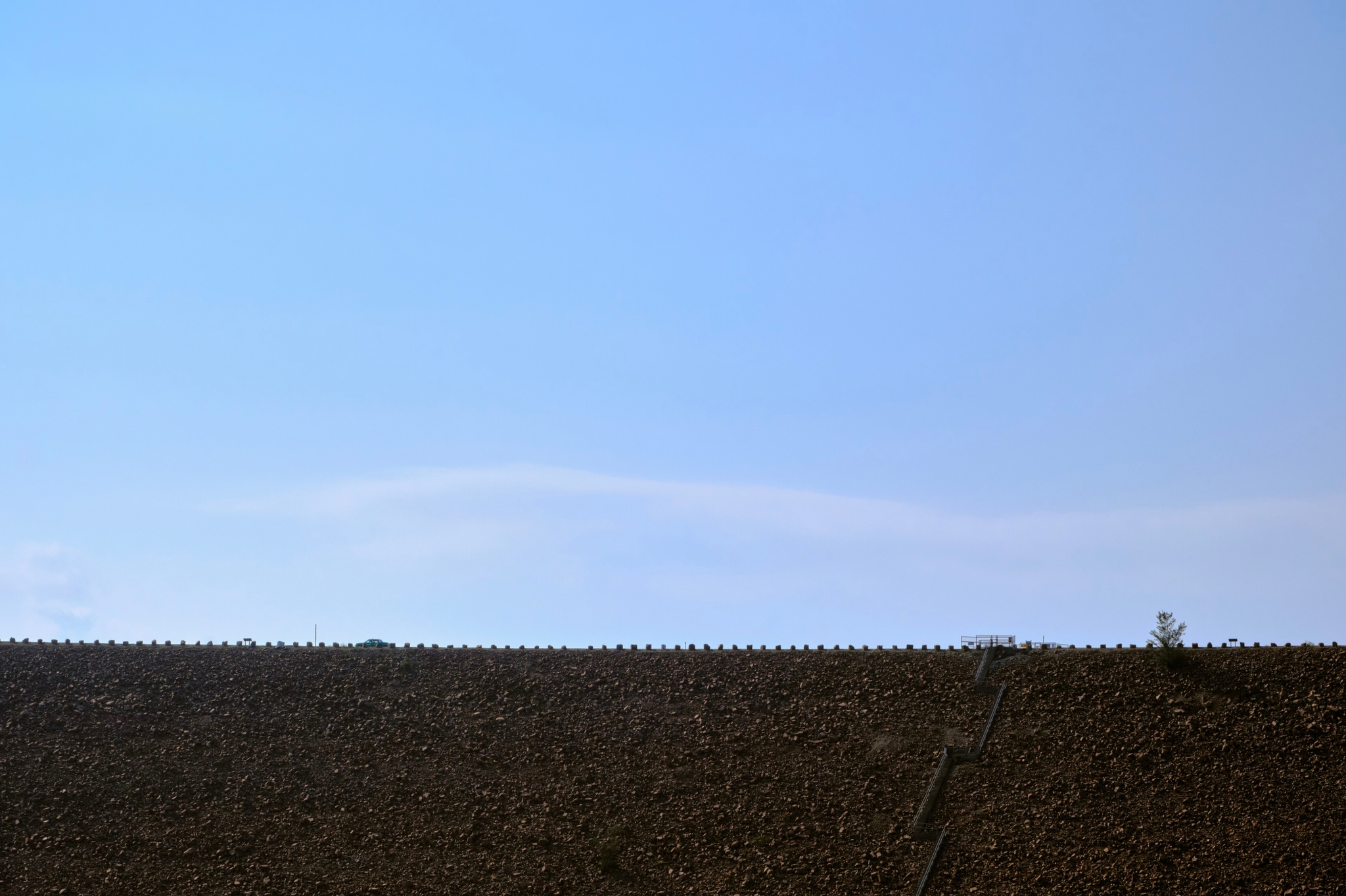 Clear blue sky above dark, flat horizon line with subtle white cloud and tiny distant tree