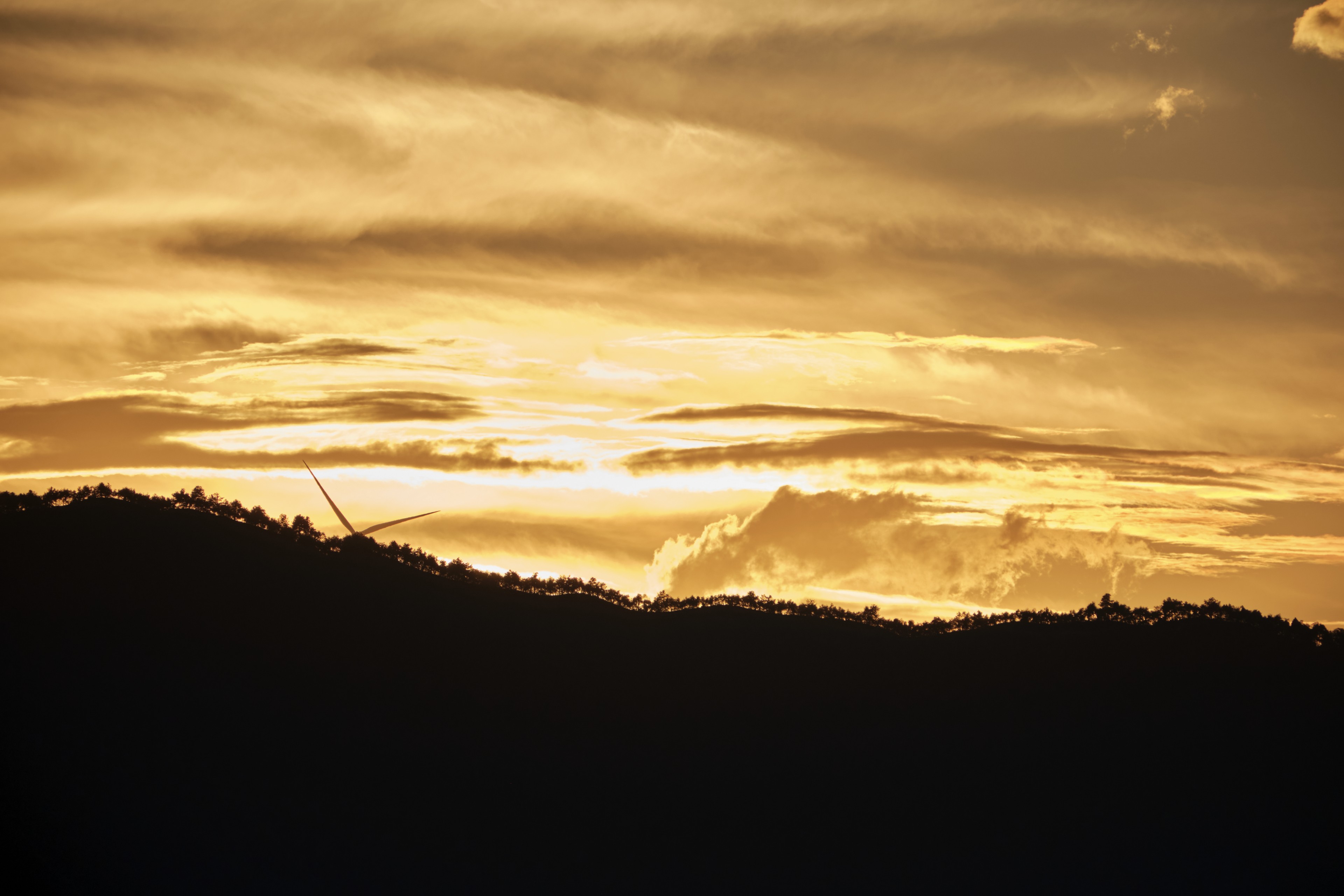 Dark silhouette of rolling hills under a golden sunset sky with luminous clouds