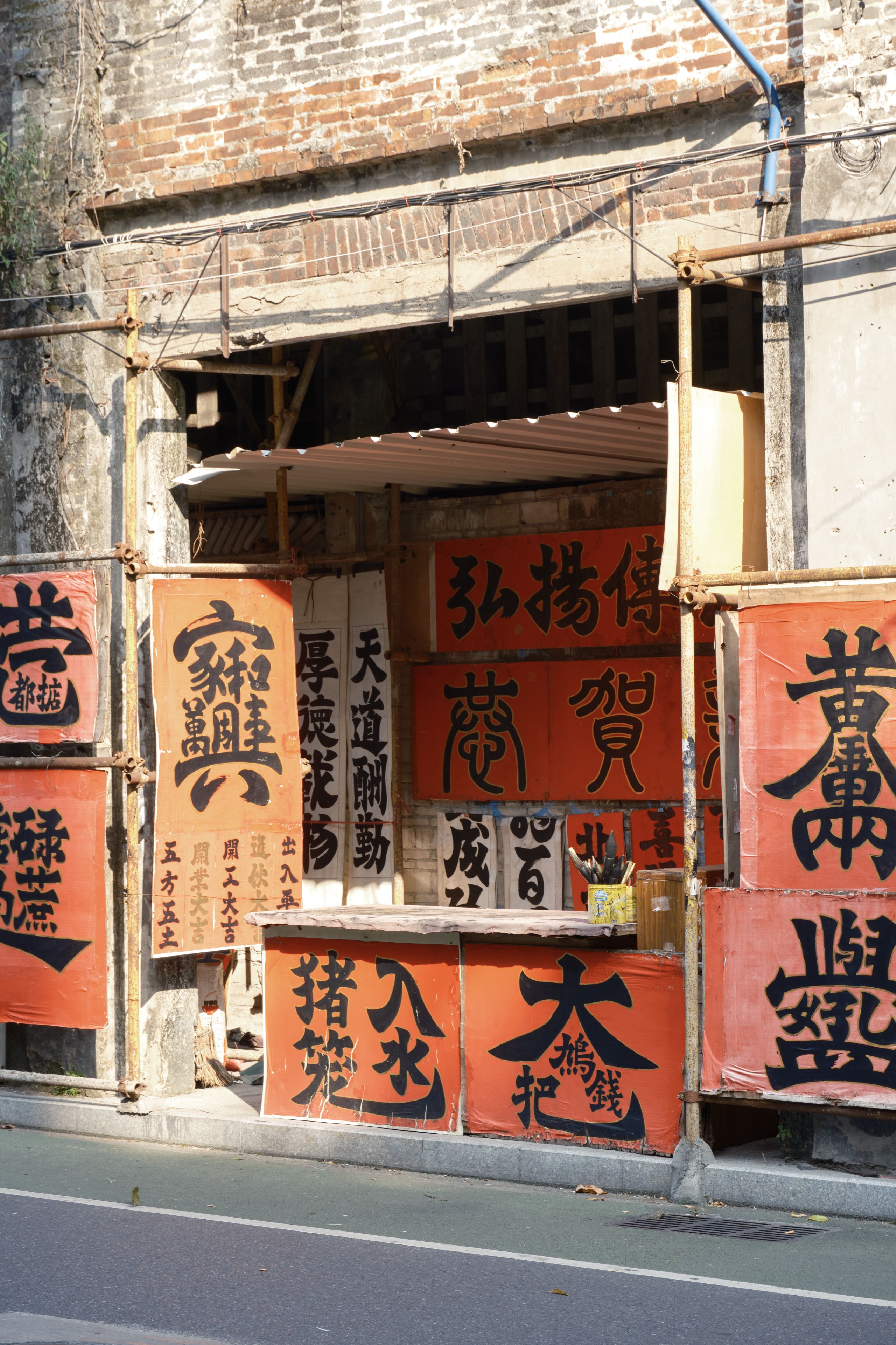 Brick building storefront adorned with red banners featuring black Chinese calligraphy and visible scaffolding