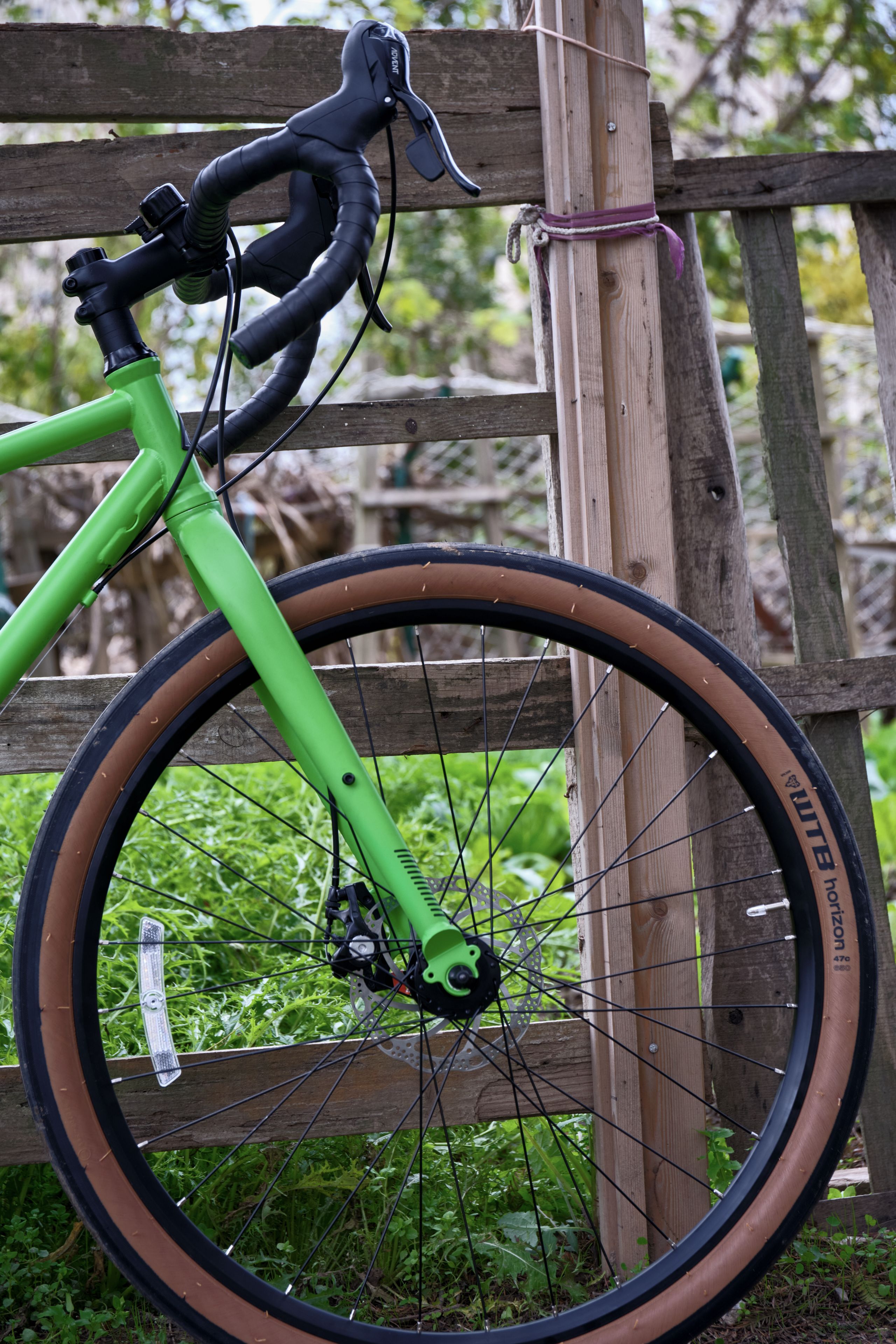 Bright green bicycle front leaning against wooden fence with tan tires