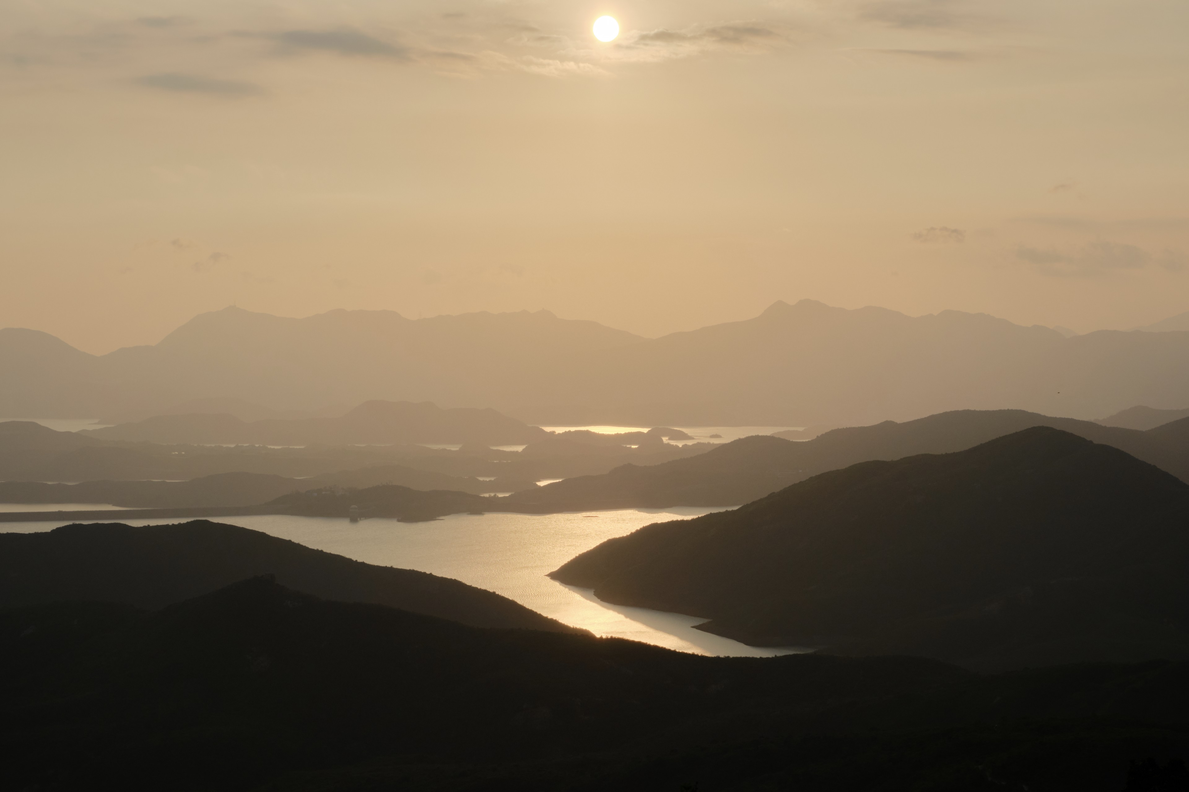 Sun over hazy mountainous landscape with winding water body