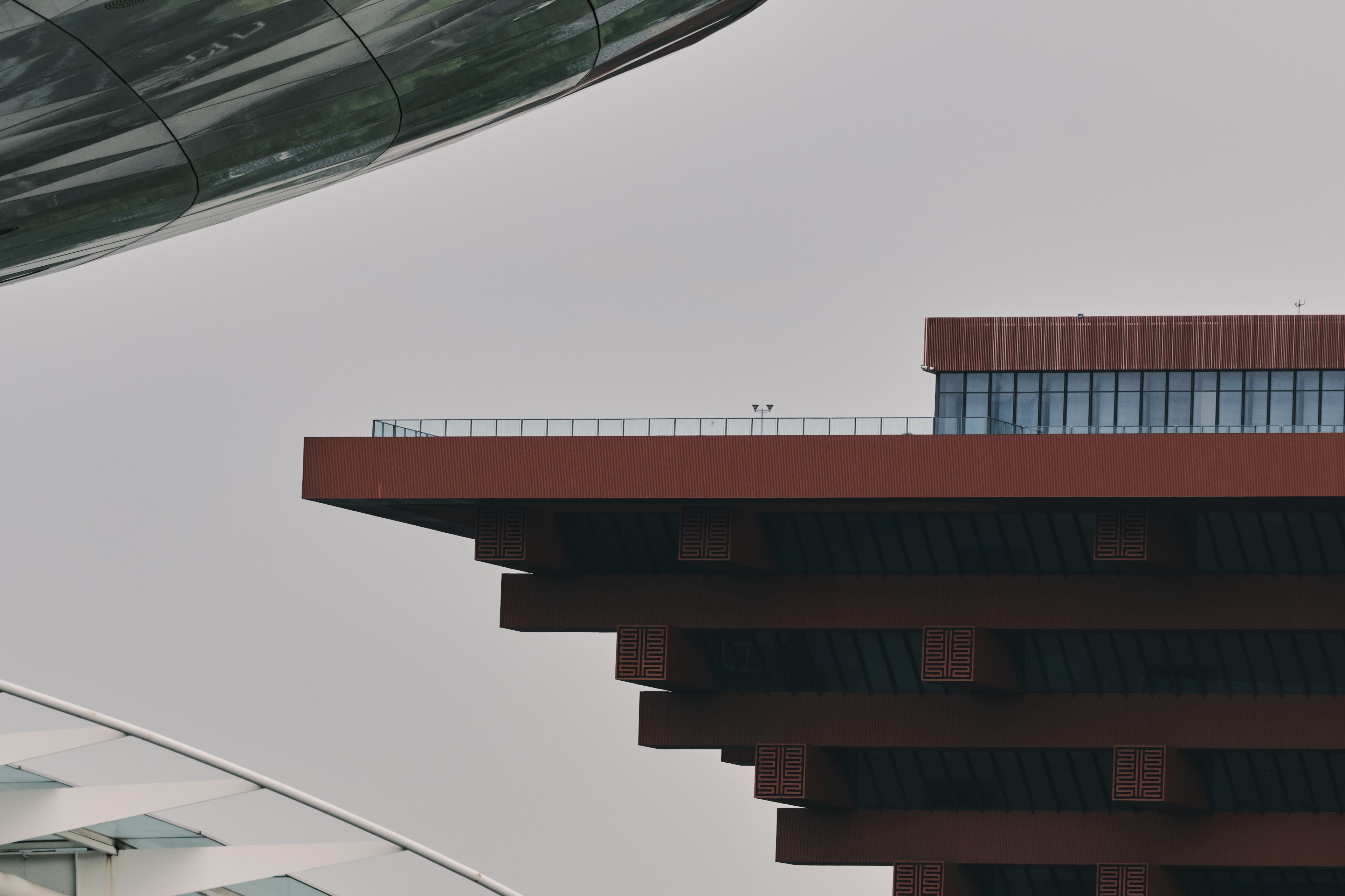 Red tiered building, curved metallic structure, grey sky