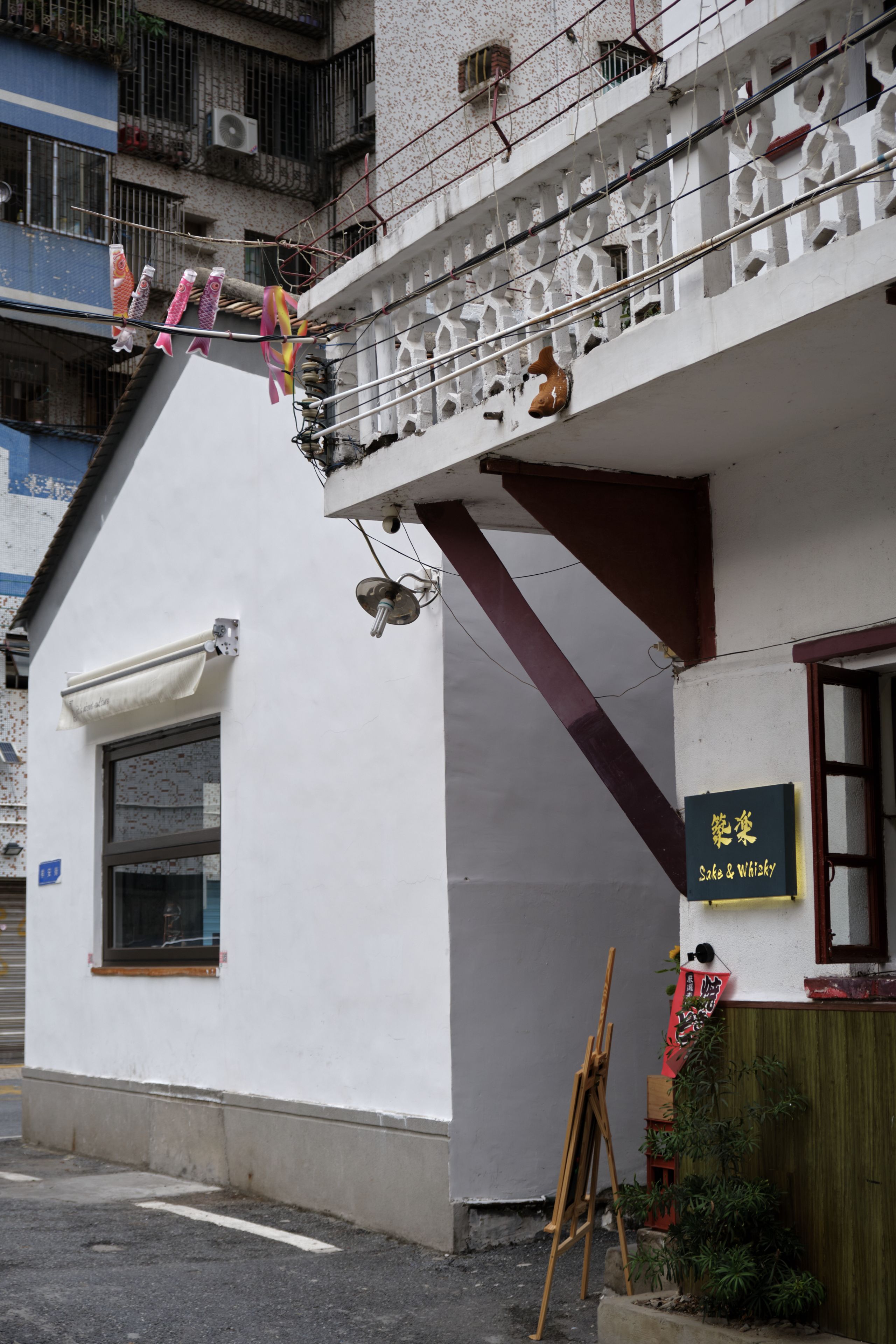 White building with clothesline and balcony in narrow urban alley, dark window, small sign