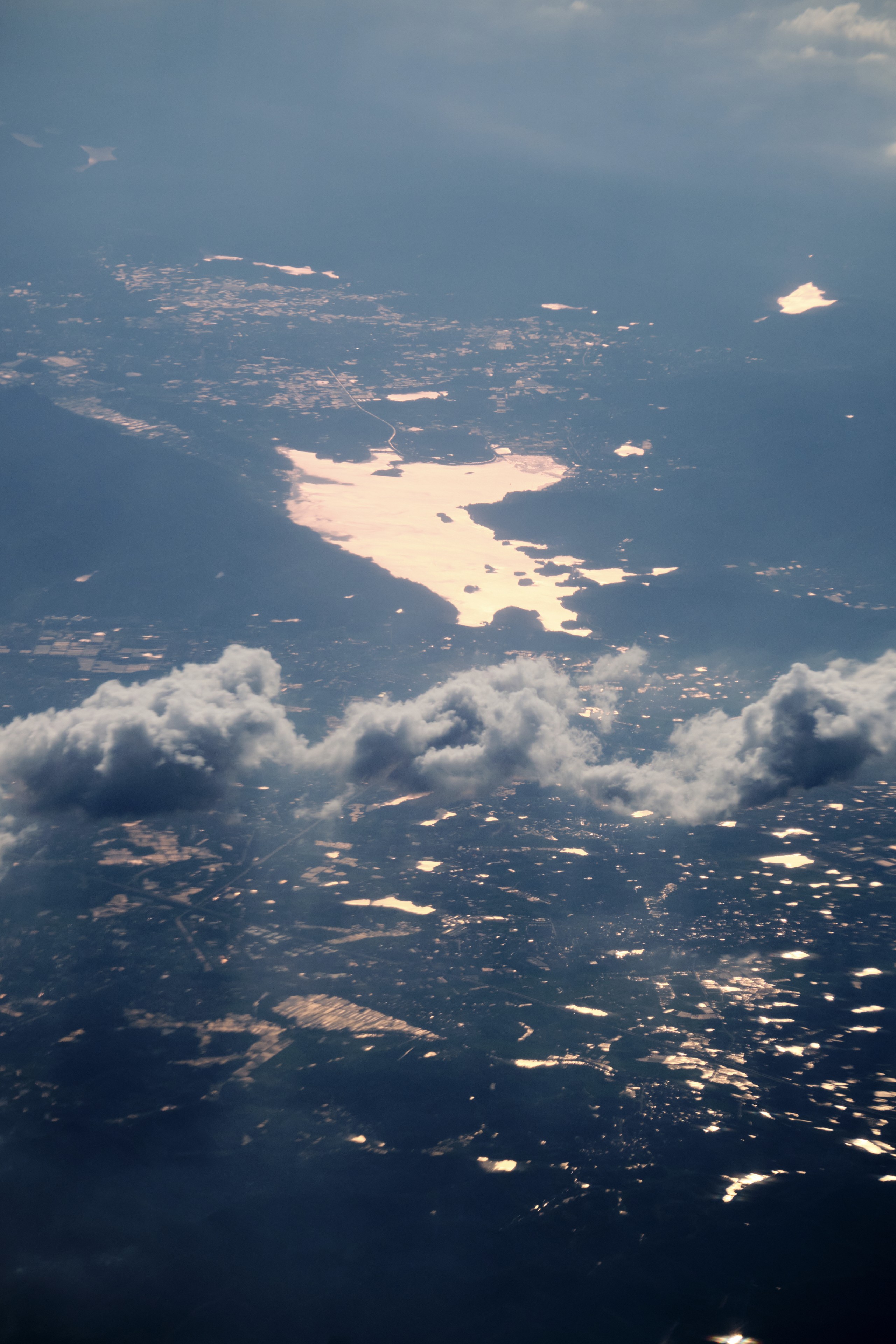Aerial view of a landscape with a large water body reflecting warm light, surrounded by numerous smaller illuminated areas on the ground and scattered clouds above