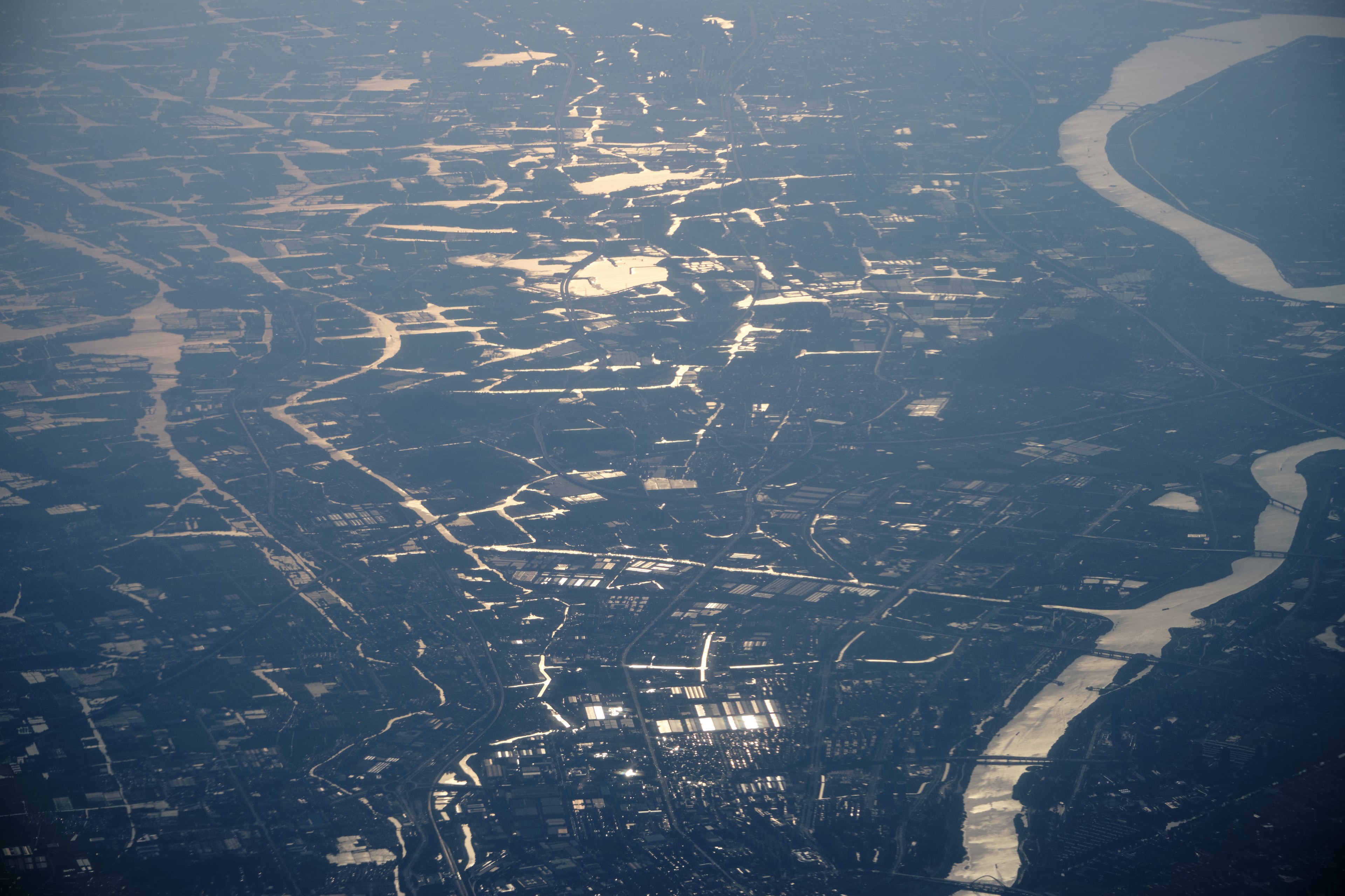 Aerial view of a city with a wide winding river, dense green areas, and scattered urban structures