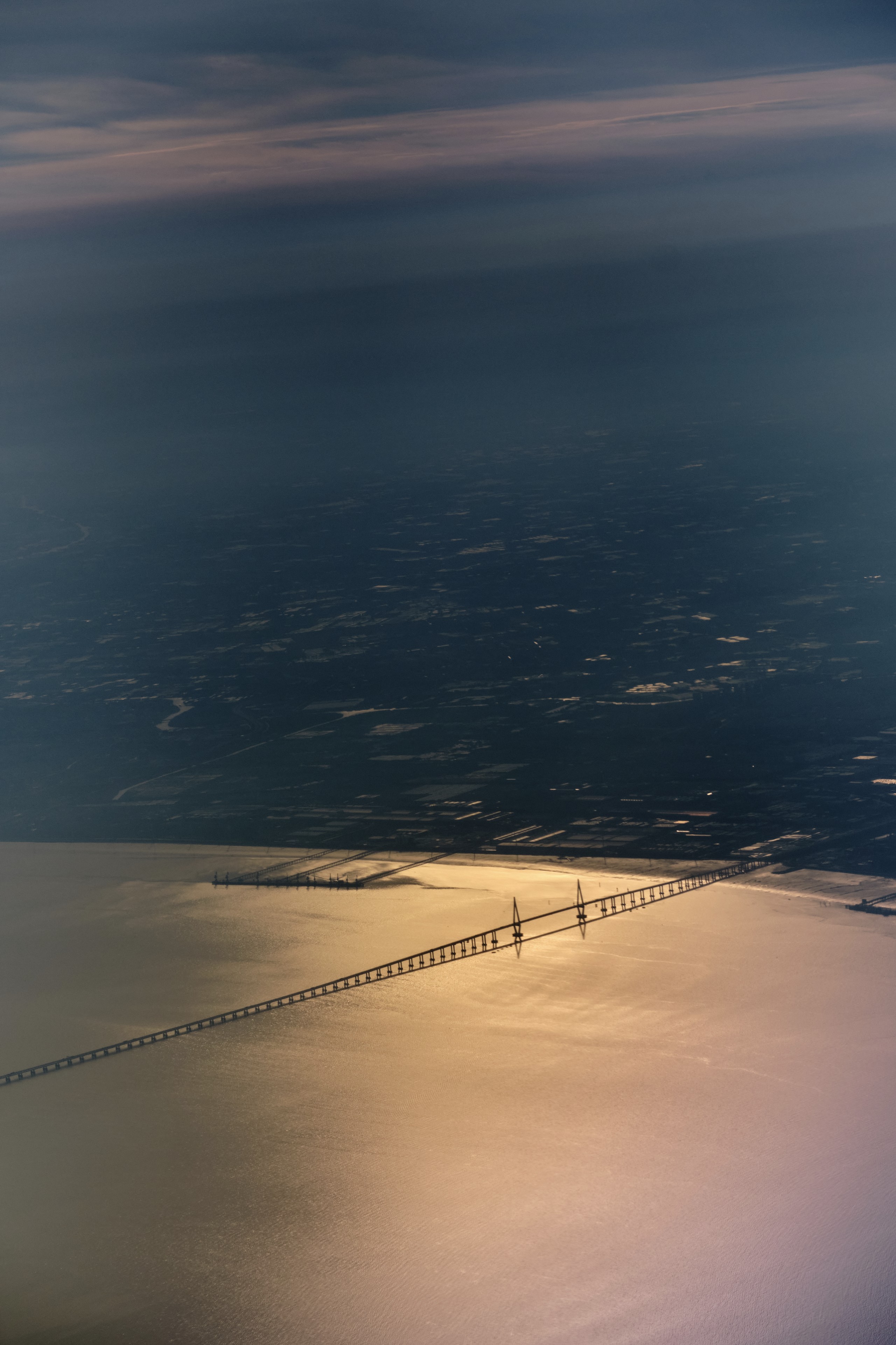 Aerial view of a long bridge over sun-dappled water with dark distant land