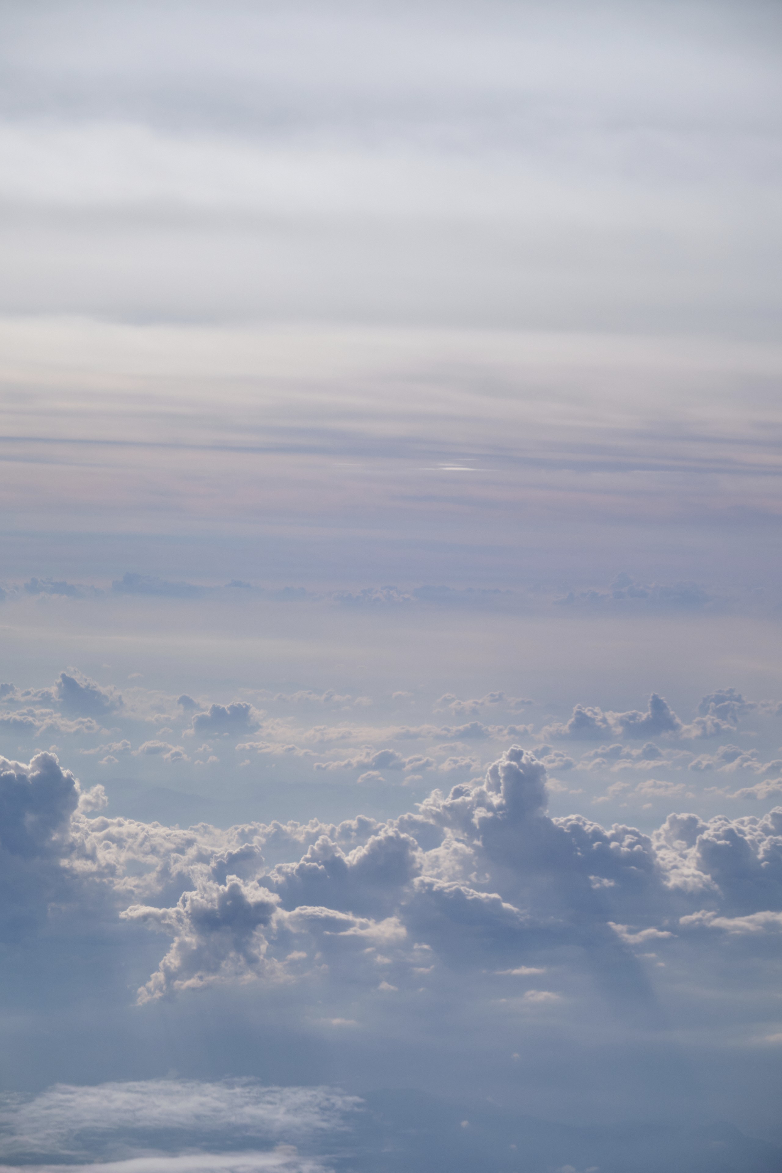 Aerial view of layered white and grey clouds under a bright, light-blue sky