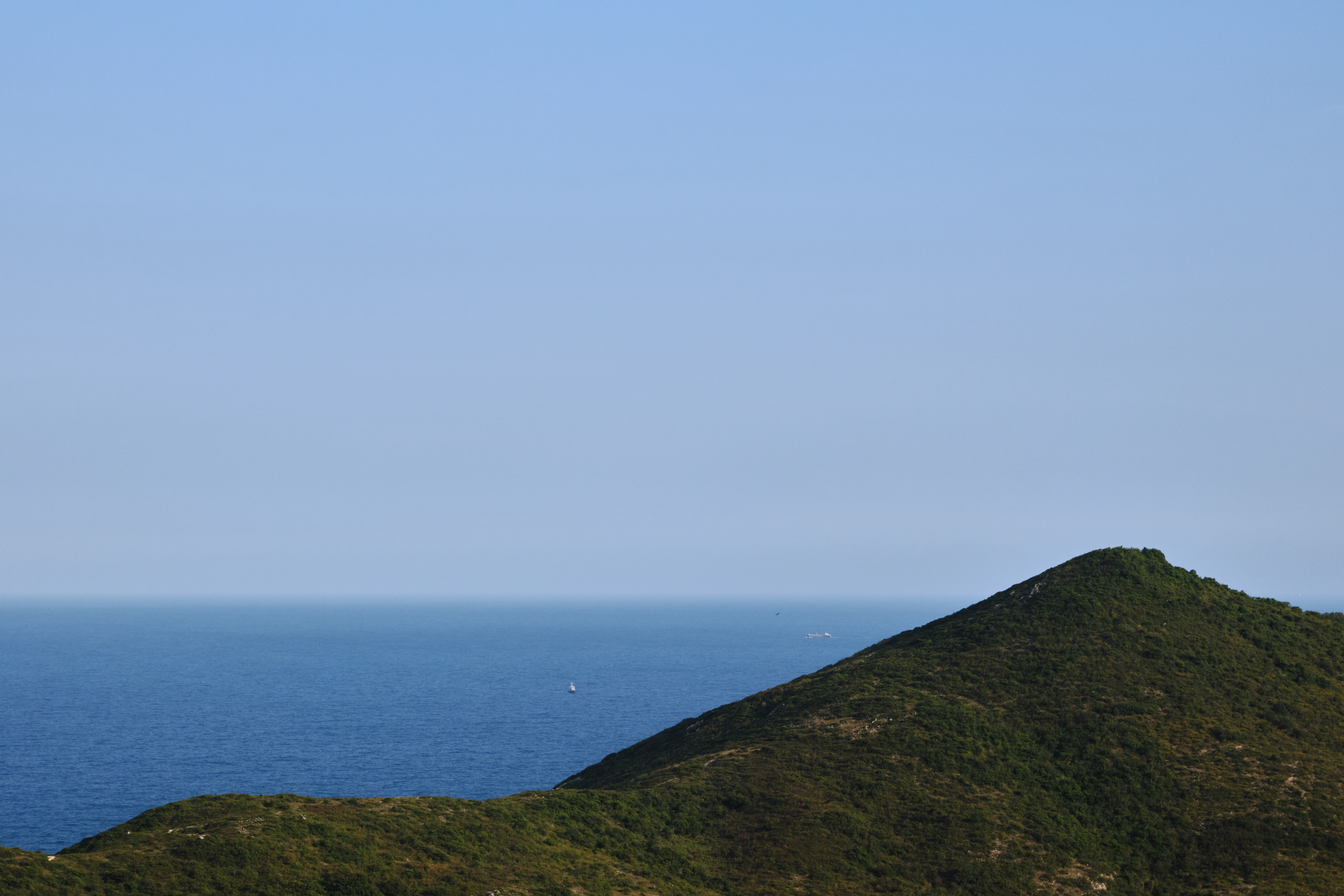 Green mountain slope, blue ocean, light blue sky