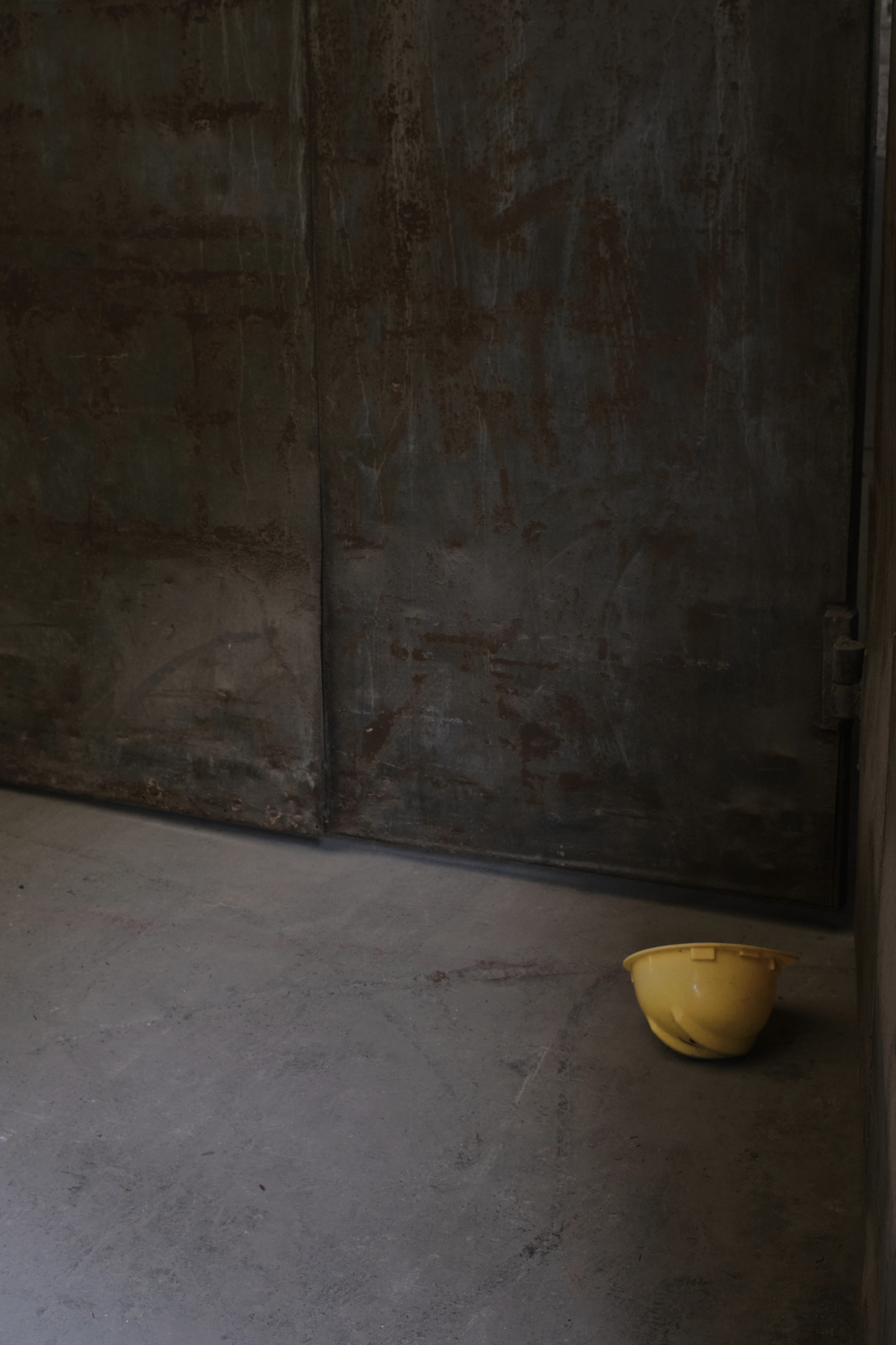 A yellow hard hat rests on the floor in a room with weathered metal walls
