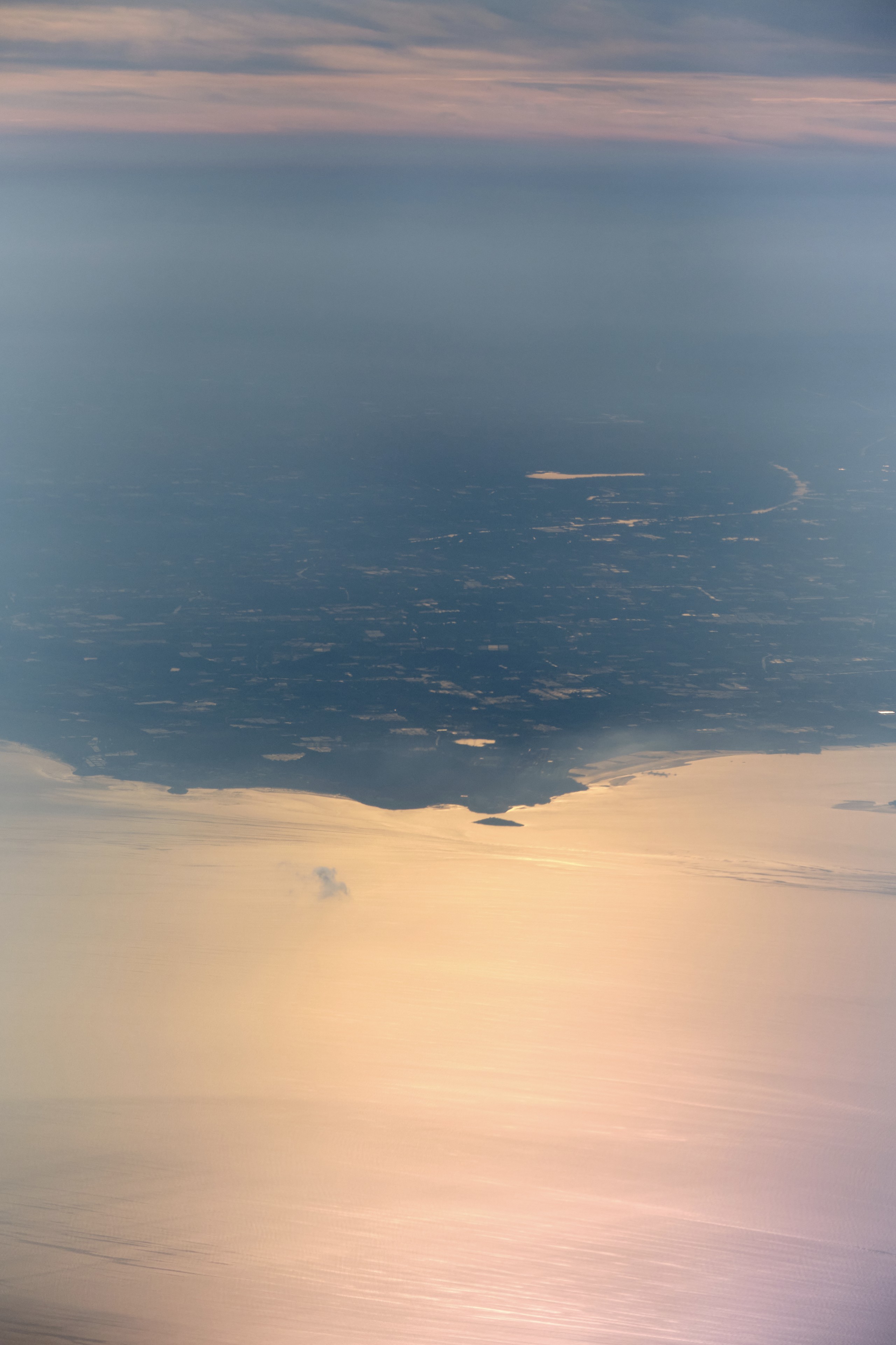 Aerial view of land meeting sunlit water under hazy sky