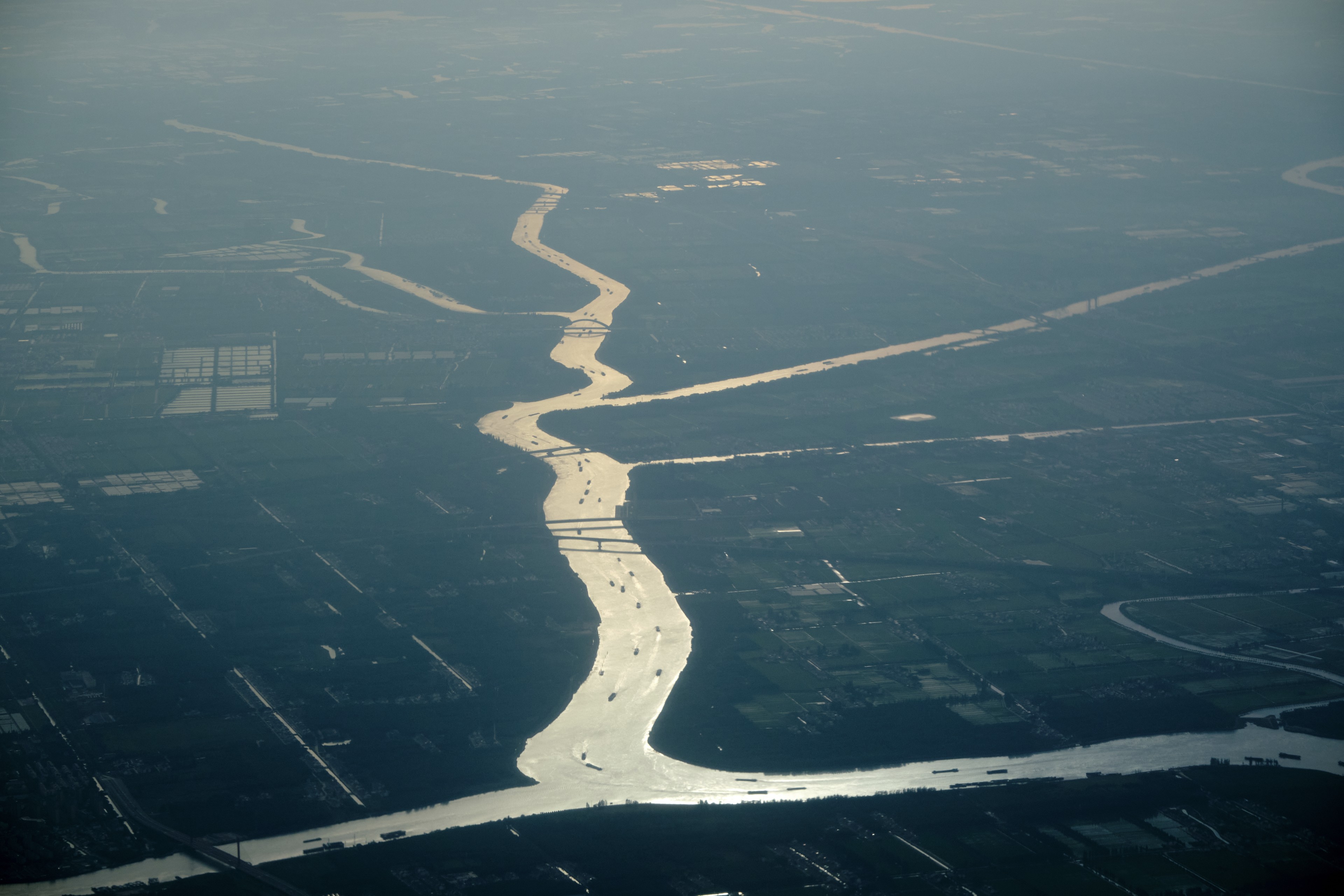 Aerial view of a winding, reflective river flowing through a hazy, dark landscape