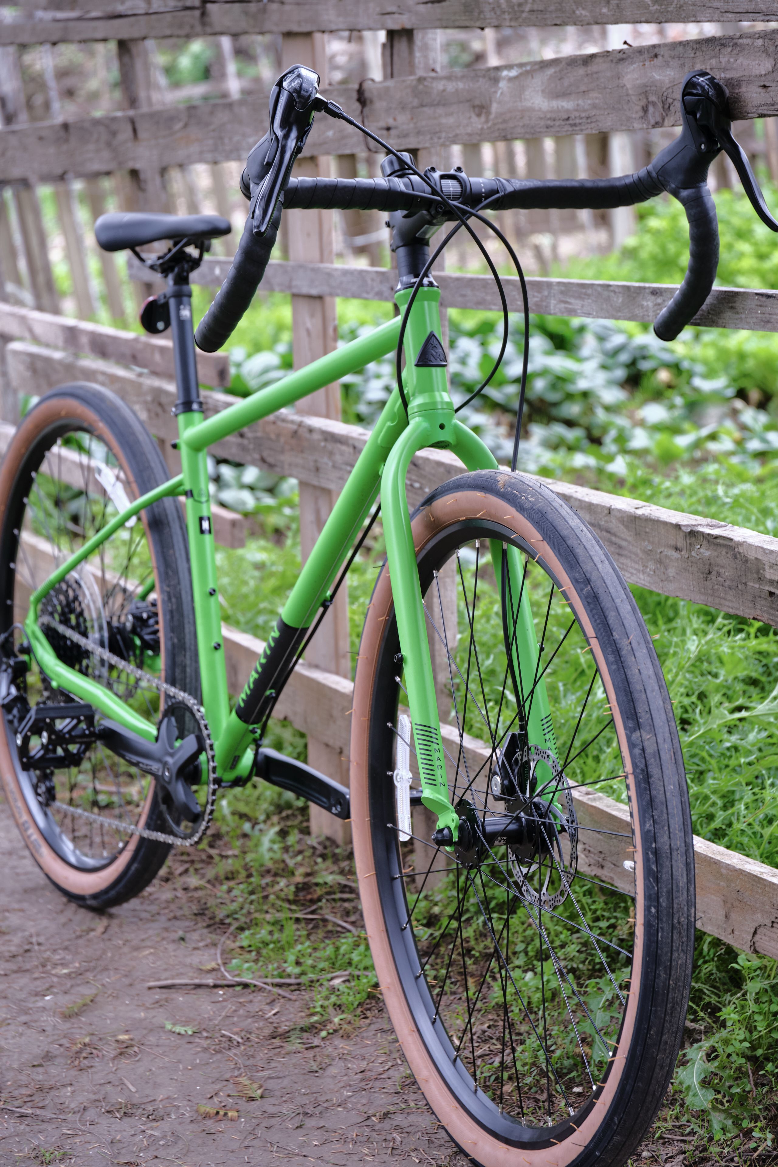 Bright green gravel bike leaning against a wooden fence