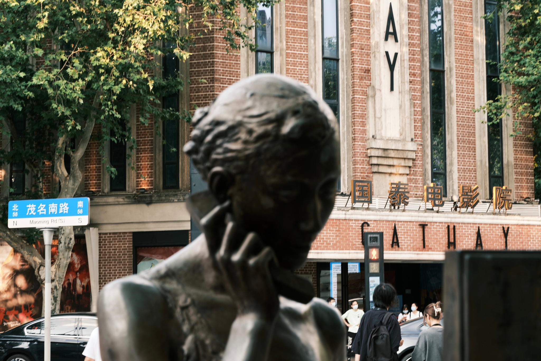 Bronze statue of woman, hand to jaw, against brick building and trees