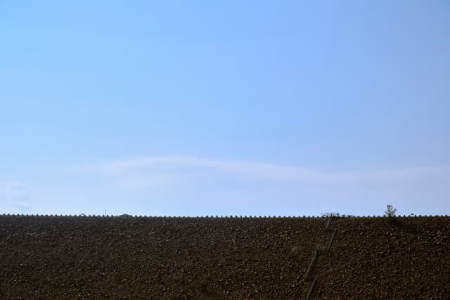 Clear blue sky above dark, flat horizon line with subtle white cloud and tiny distant tree