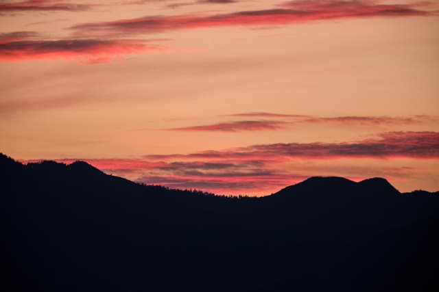 Dark mountain silhouettes against a vibrant sunset sky with red and orange clouds