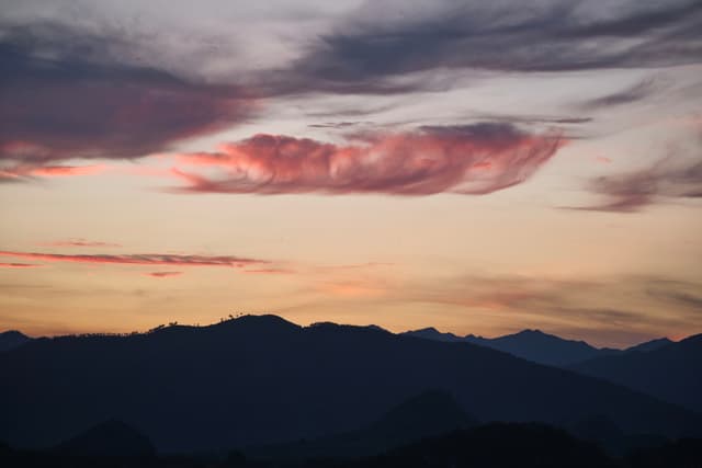 Silhouetted mountains beneath a twilight sky with a central pink cloud