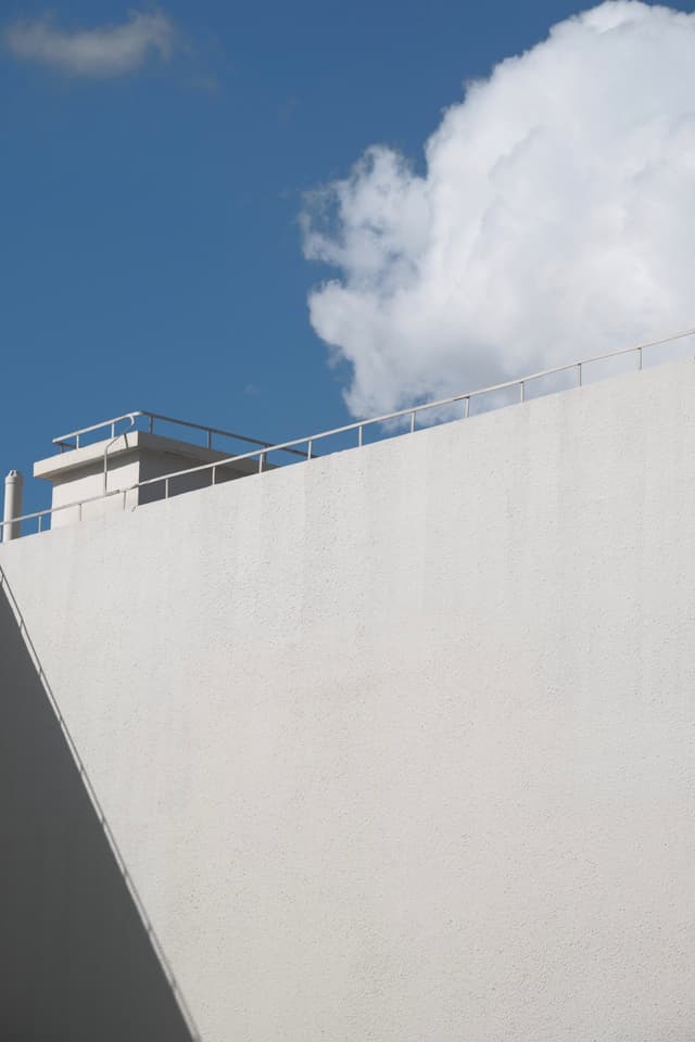 White concrete building facade against blue sky with large white cloud
