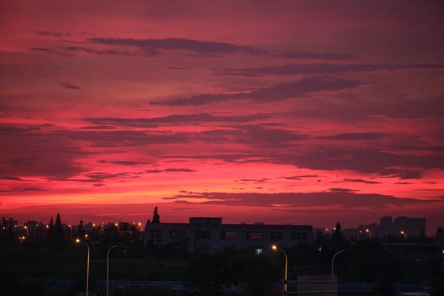 City skyline silhouetted against a vibrant red and pink sunset sky with scattered clouds and illuminated streetlights