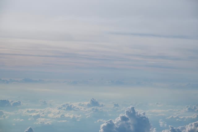 Layered clouds from above, pale blue-grey sky dominating the frame