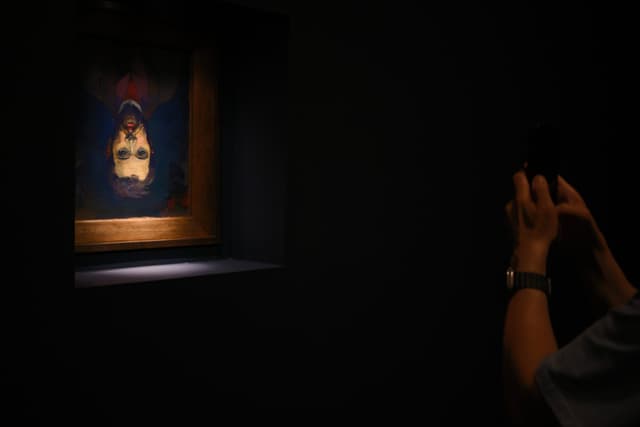 A person takes a photo of an illuminated, upside-down portrait in a dark museum room