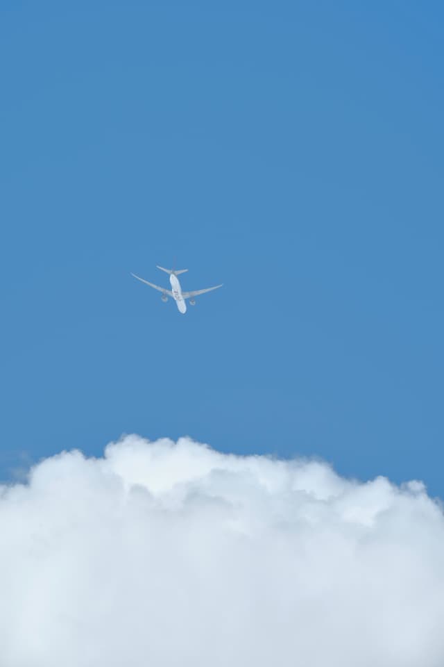 White airplane flying above clouds in a blue sky