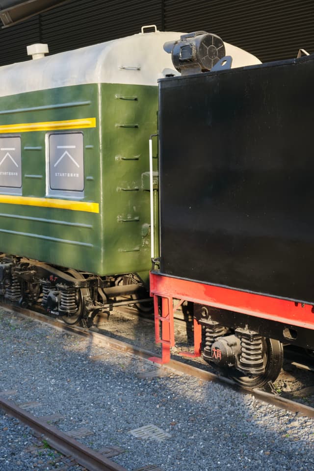 Black train engine car coupled with a green and white passenger coach on gravel tracks