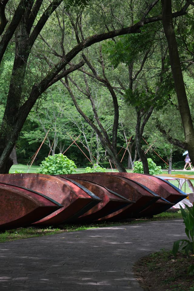 Row of five red overturned boats on a path beneath green trees