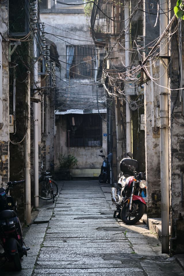 Narrow, vertical view of a densely wired alleyway with parked motorcycles and bicycles between old buildings