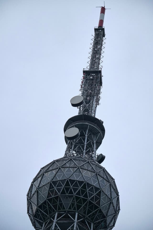 Close-up of a tall steel transmission tower's spherical observation deck and an antenna mast extending against an overcast sky