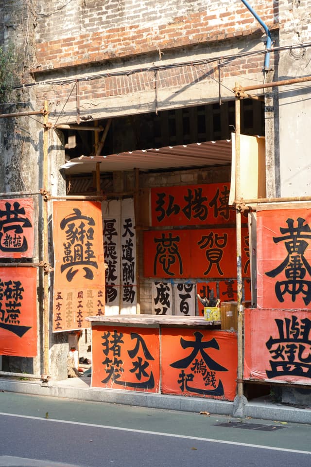 Brick building storefront adorned with red banners featuring black Chinese calligraphy and visible scaffolding