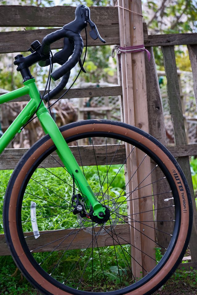 Bright green bicycle front leaning against wooden fence with tan tires