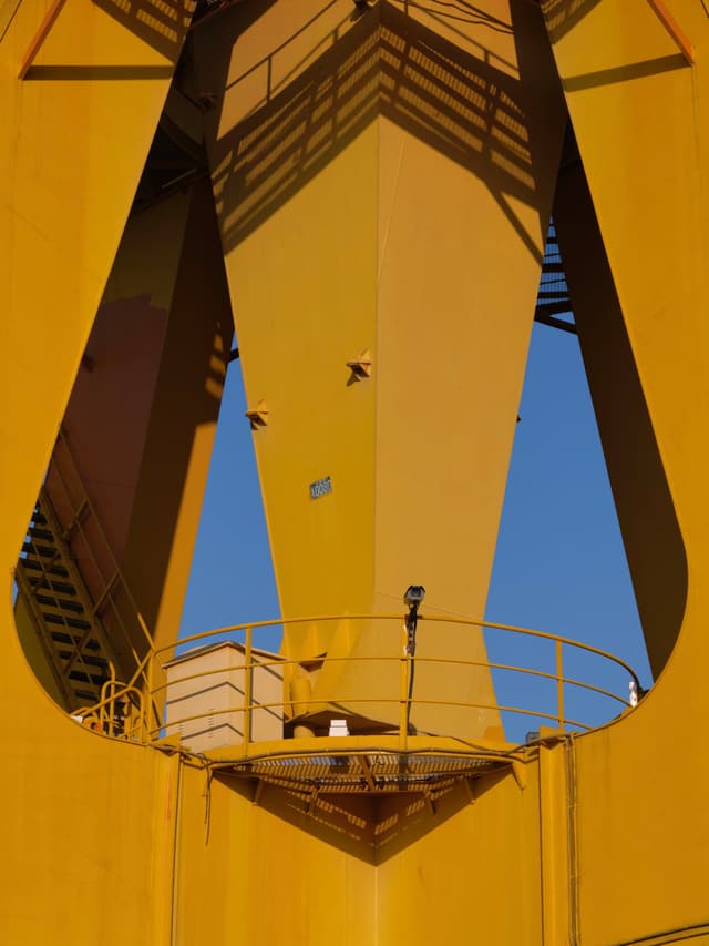 Yellow industrial structure framing blue sky, small birds, circular platform, and shadows
