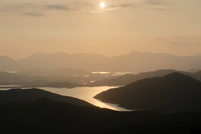 Sun over hazy mountainous landscape with winding water body