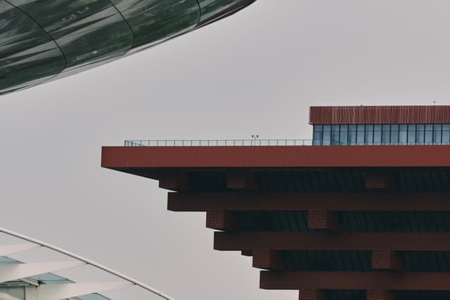 Red tiered building, curved metallic structure, grey sky