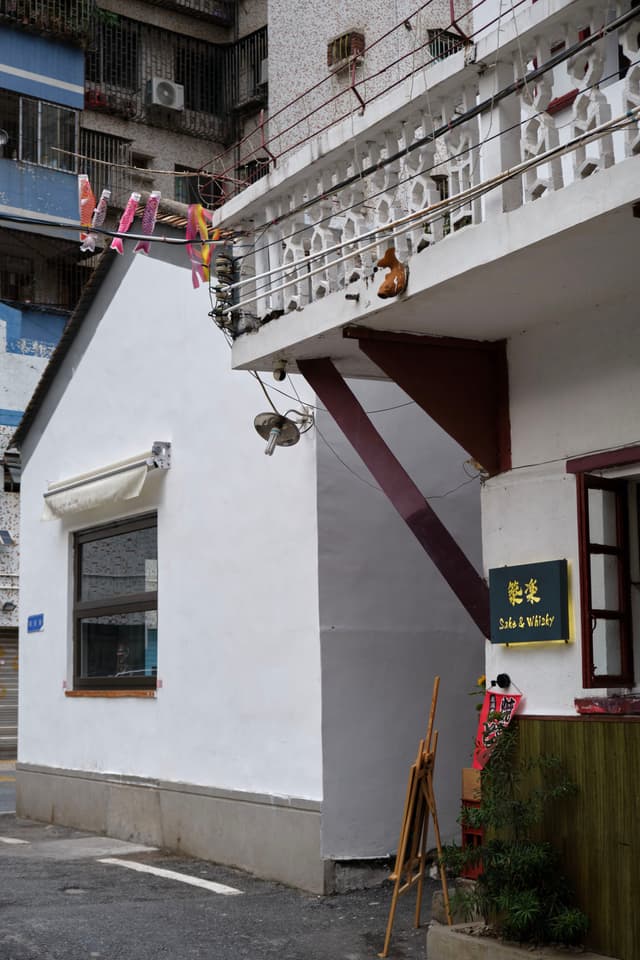 White building with clothesline and balcony in narrow urban alley, dark window, small sign