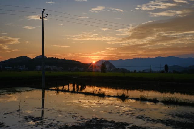 Sunset over mountains, utility pole reflecting in dark water, power lines overhead
