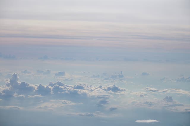 Aerial view of multiple layers of soft cumulus clouds under a pale, diffused sky