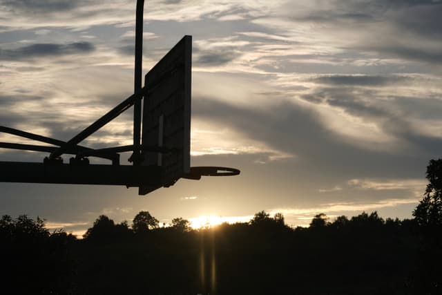 Silhouetted basketball hoop against a cloudy sunset sky