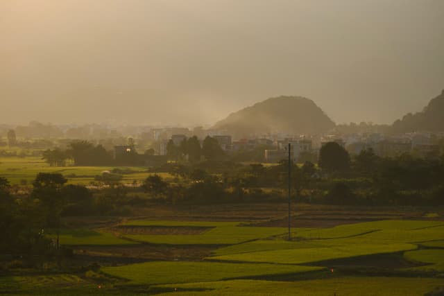 Hazy landscape with green fields, distant town, and hills under golden light