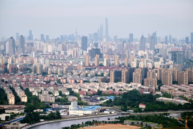 Expansive cityscape featuring dense buildings, a winding river, and distant hazy skyline