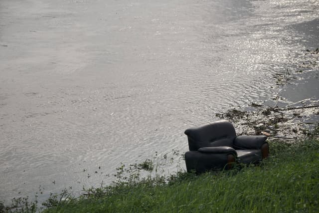 Dark armchair on grassy bank beside rippled water