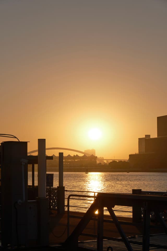 Orange sunset over water with silhouetted city and pier