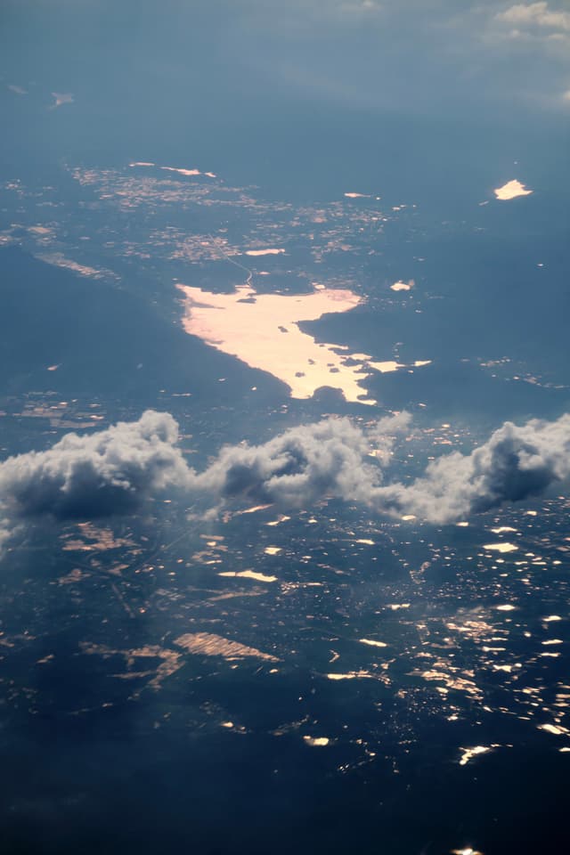 Aerial view of a landscape with a large water body reflecting warm light, surrounded by numerous smaller illuminated areas on the ground and scattered clouds above