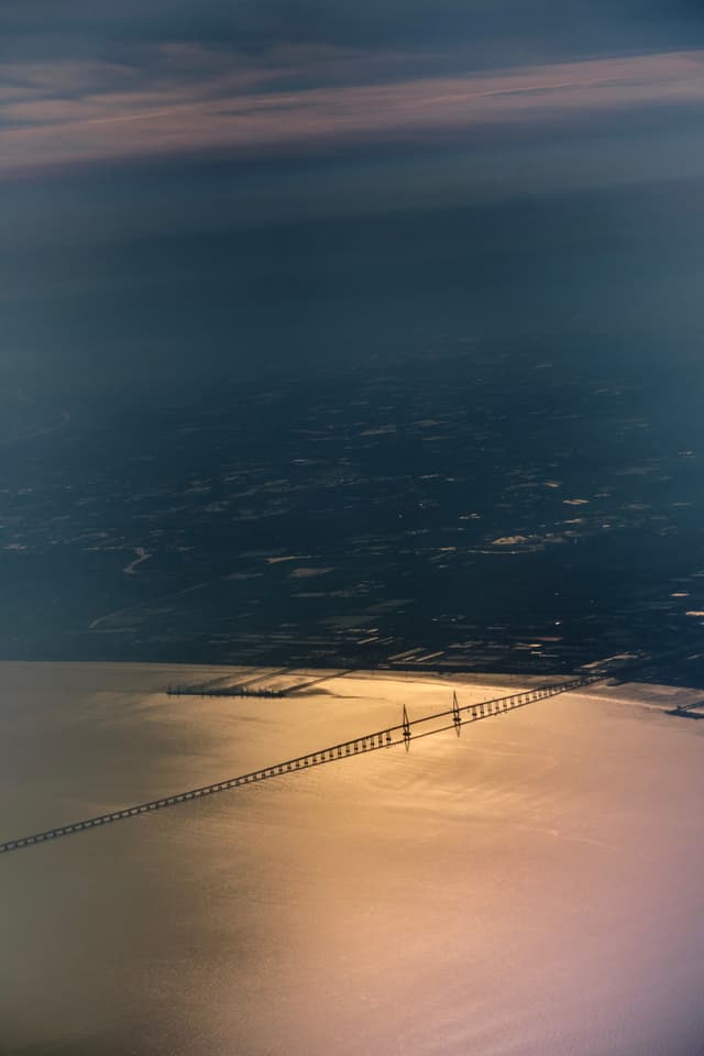 Aerial view of a long bridge over sun-dappled water with dark distant land