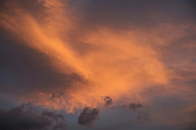 Dark gray and orange clouds fill the sky, with a bright orange cloud formation at the center