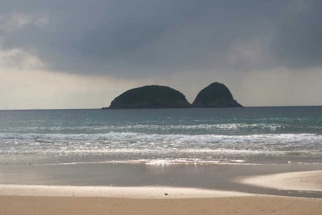 Sandy beach, ocean waves, two green islands, cloudy sky