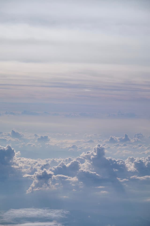 Aerial view of layered white and grey clouds under a bright, light-blue sky
