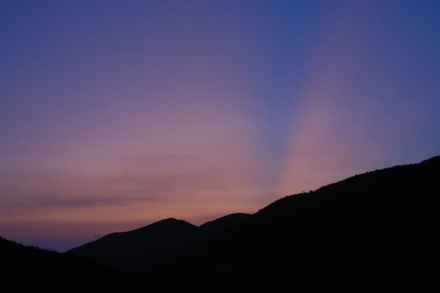 Silhouetted mountains against a twilight sky with crepuscular rays