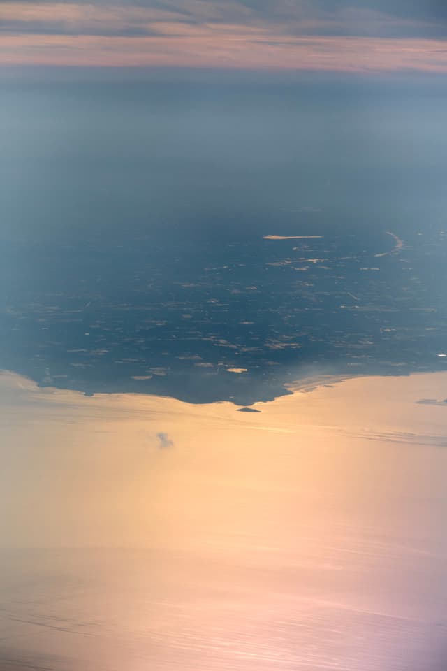 Aerial view of land meeting sunlit water under hazy sky