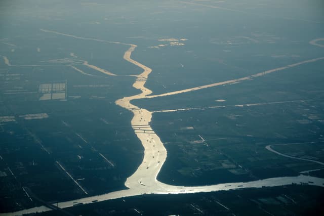 Aerial view of a winding, reflective river flowing through a hazy, dark landscape